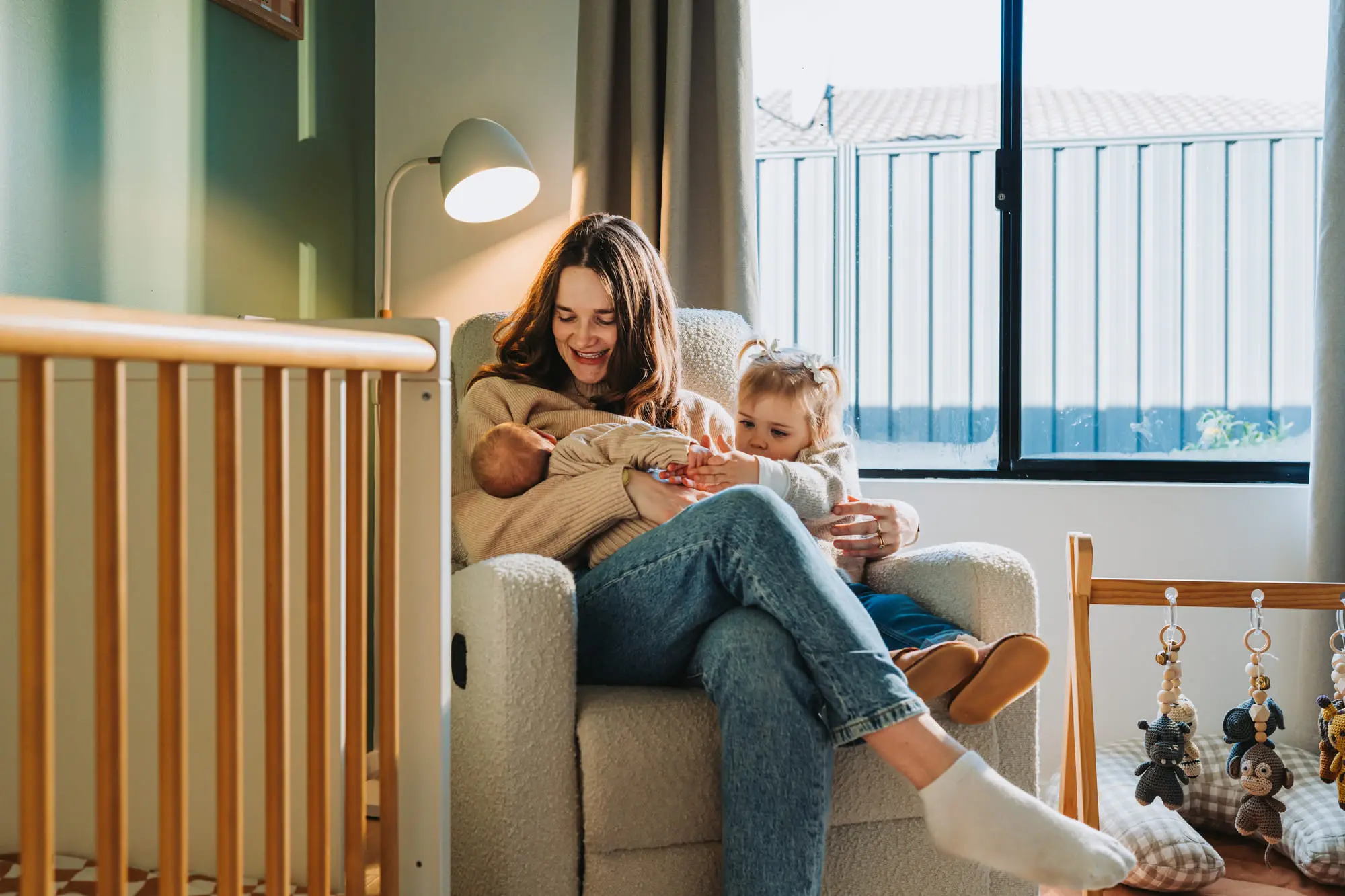 A mother with her newborn and toddler in a nursery armchair