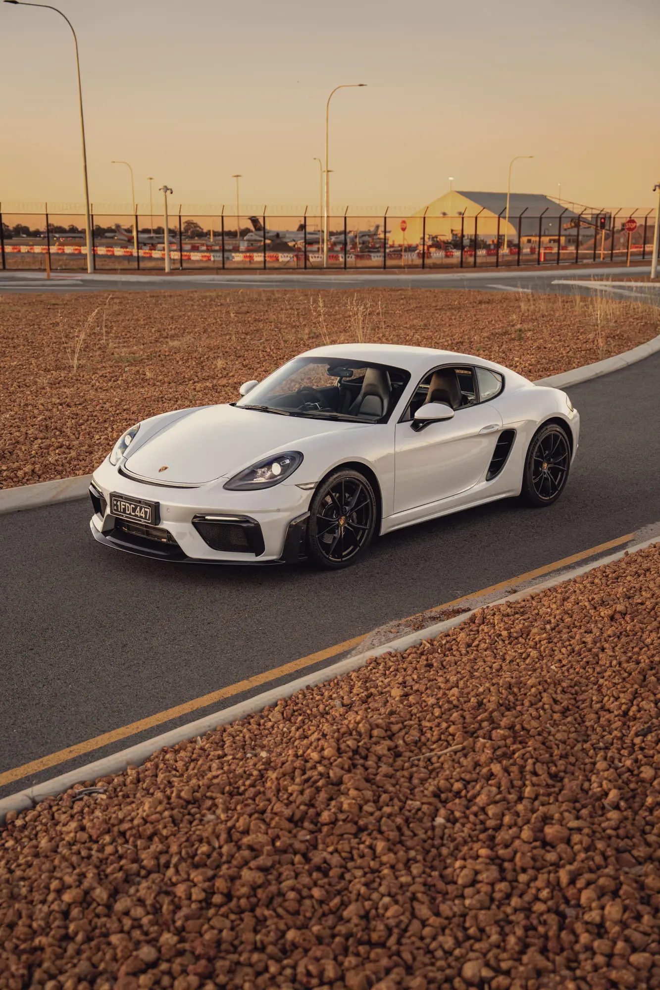 The 718 on a road curve at sunset, gravel in the foreground