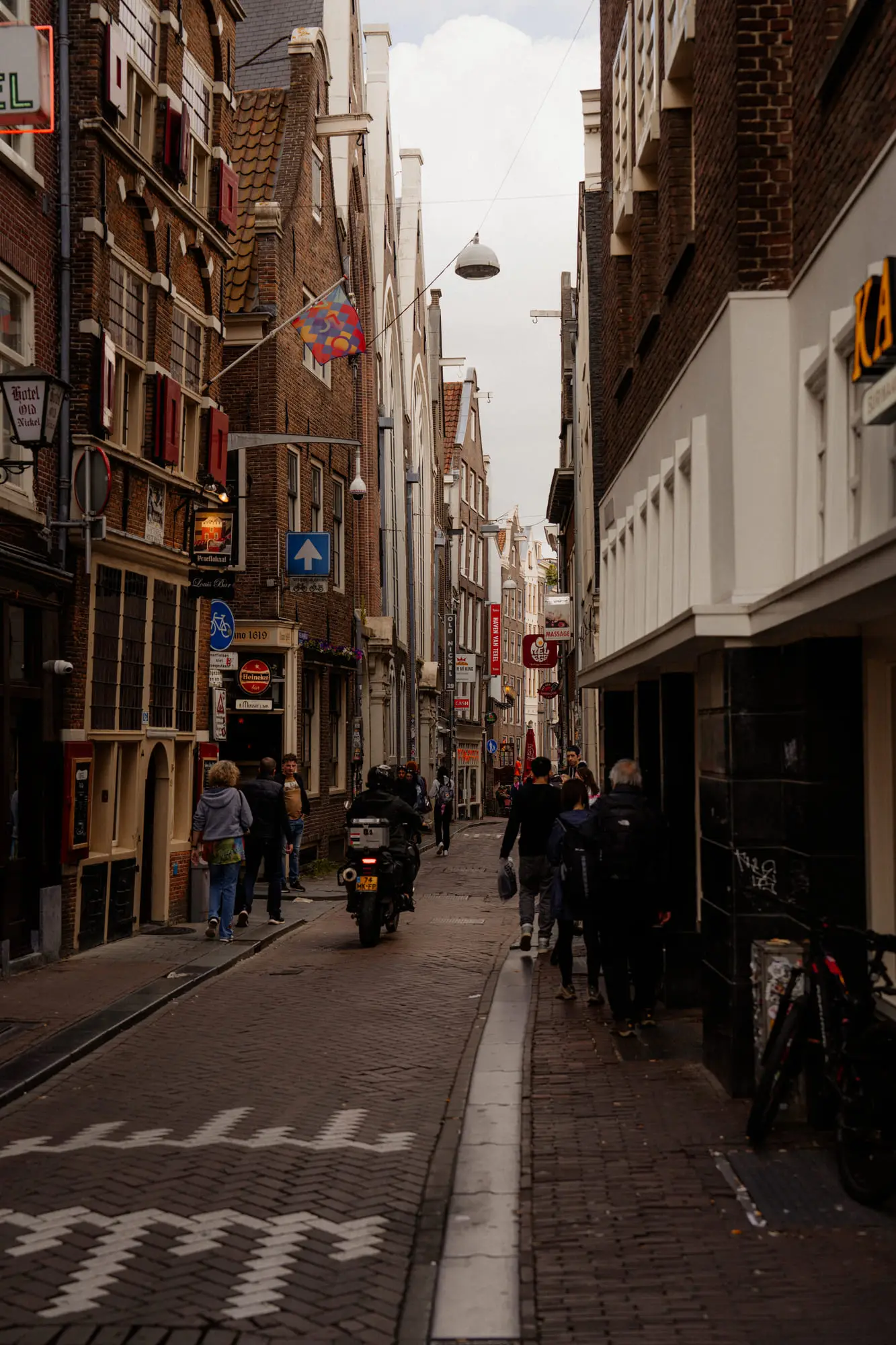 A narrow Amsterdam street, scooters and cyclists on the cobbles