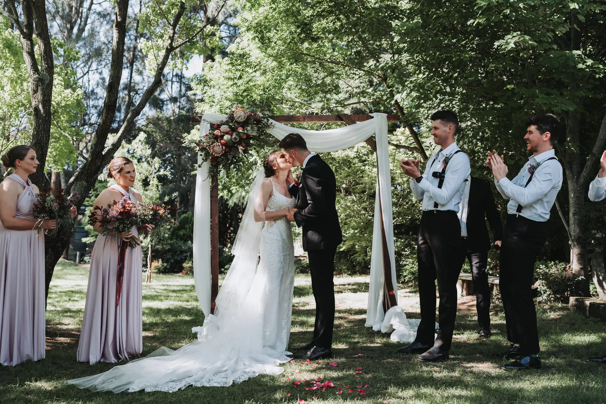 A first kiss under the arbour, the bridal party clapping