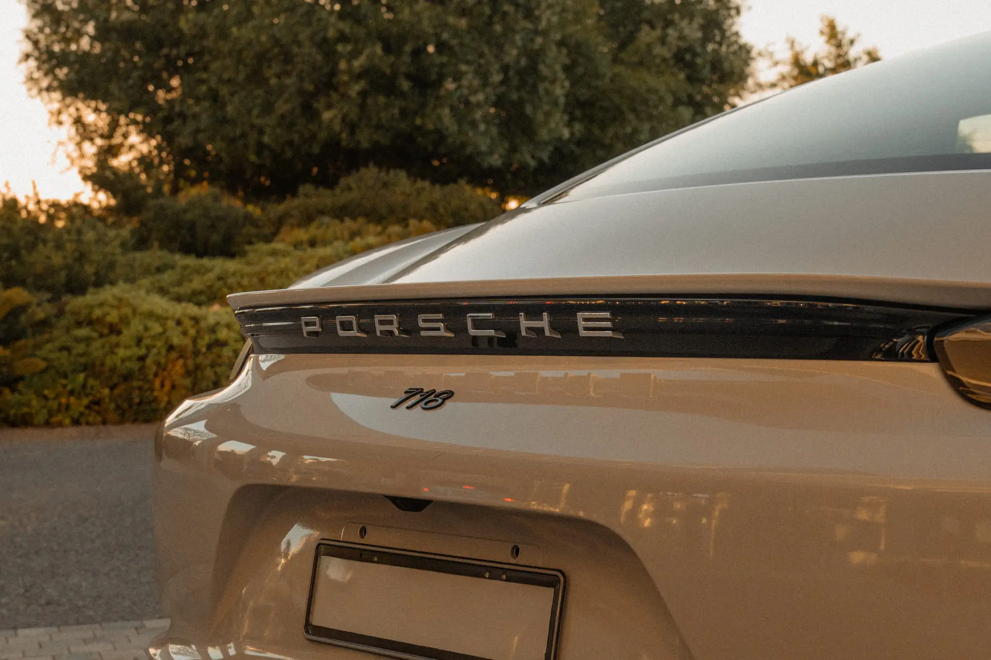 The rear of a white Porsche 718 at golden hour, the badge in focus