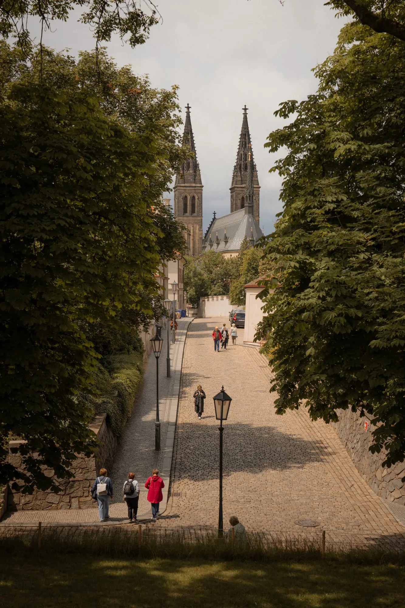 A lamplit cobbled avenue climbing toward the twin spires at Vysehrad, Prague