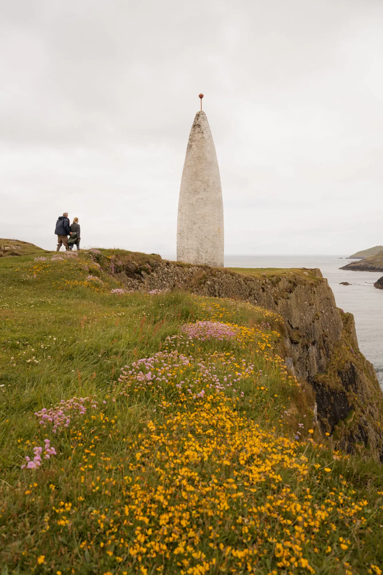 The white Baltimore Beacon on the clifftop, wildflowers and two people looking out