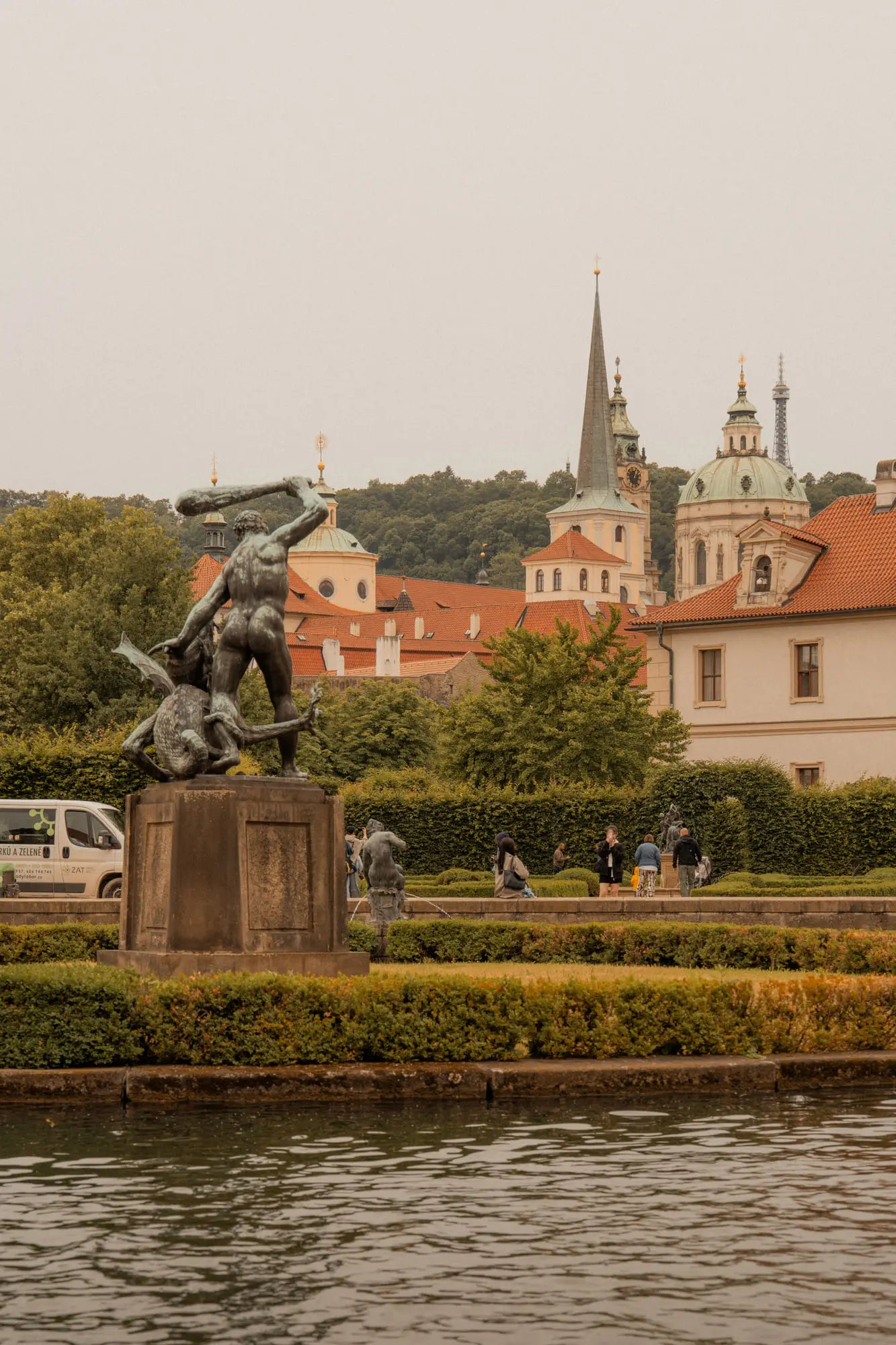 A statue in the Wallenstein Garden, a dome and spire on the skyline