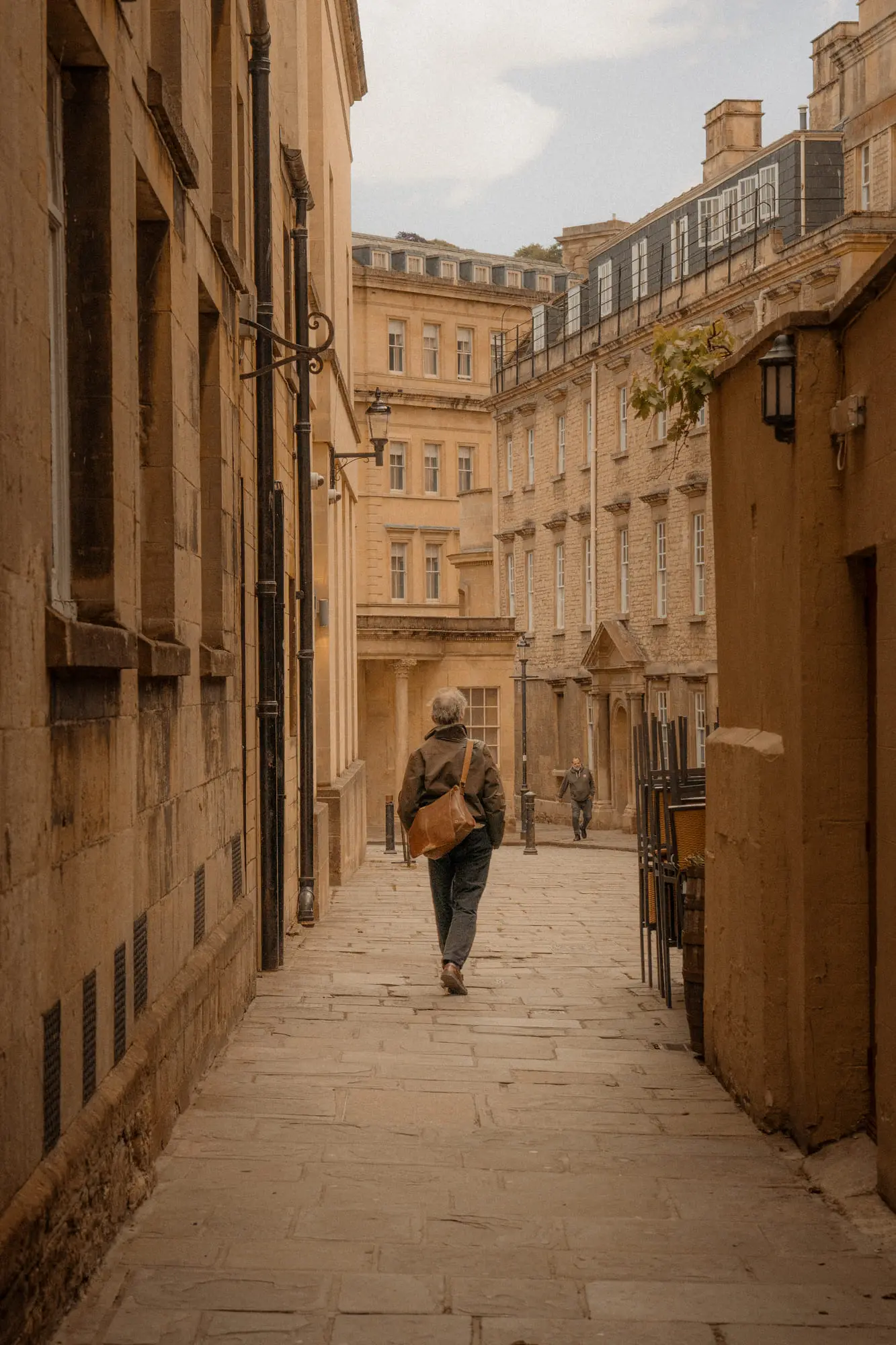 A figure walking a narrow lane between honey-stone walls, Bath