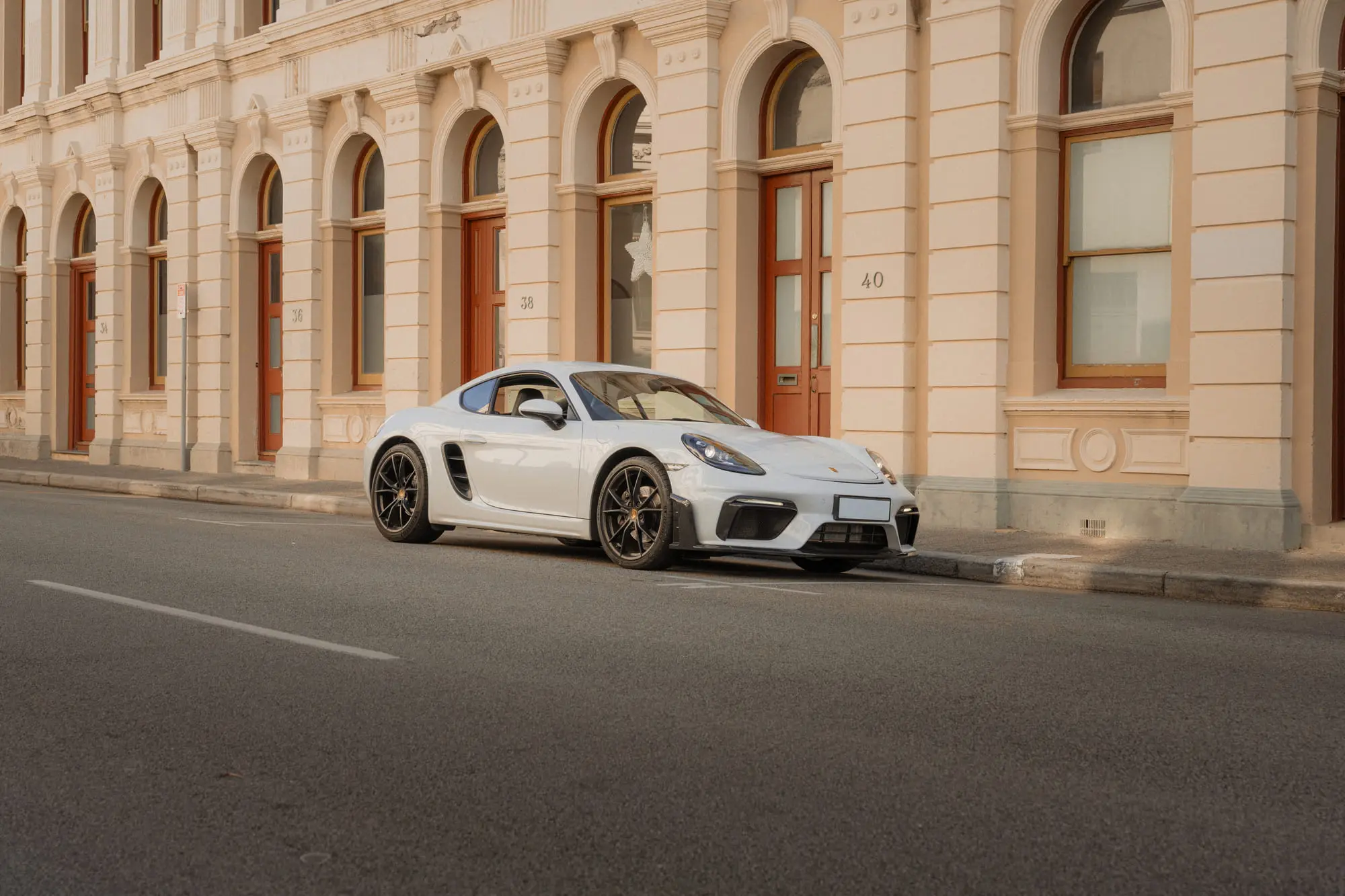 A white Porsche 718 parked on a street of arched Fremantle windows