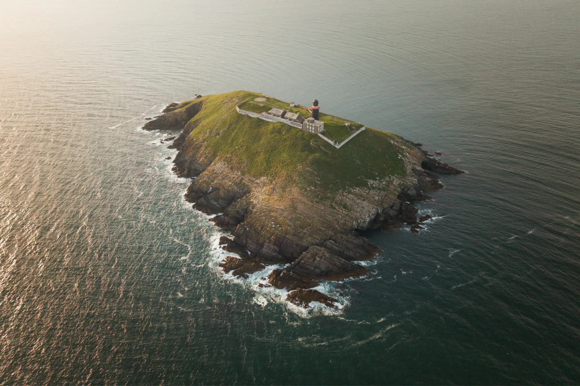 An island lighthouse catching low golden light, aerial