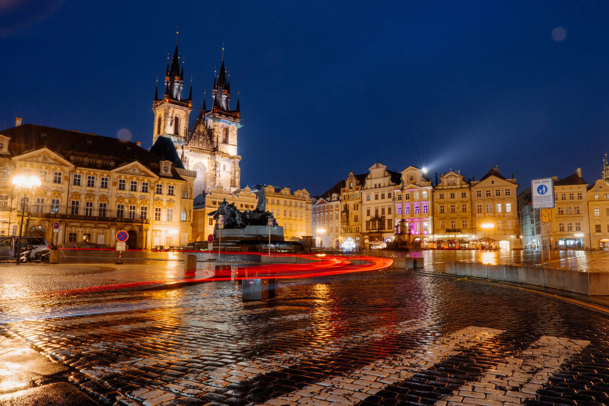 Old Town Square at night, the Tyn Church lit and light trails on wet cobbles