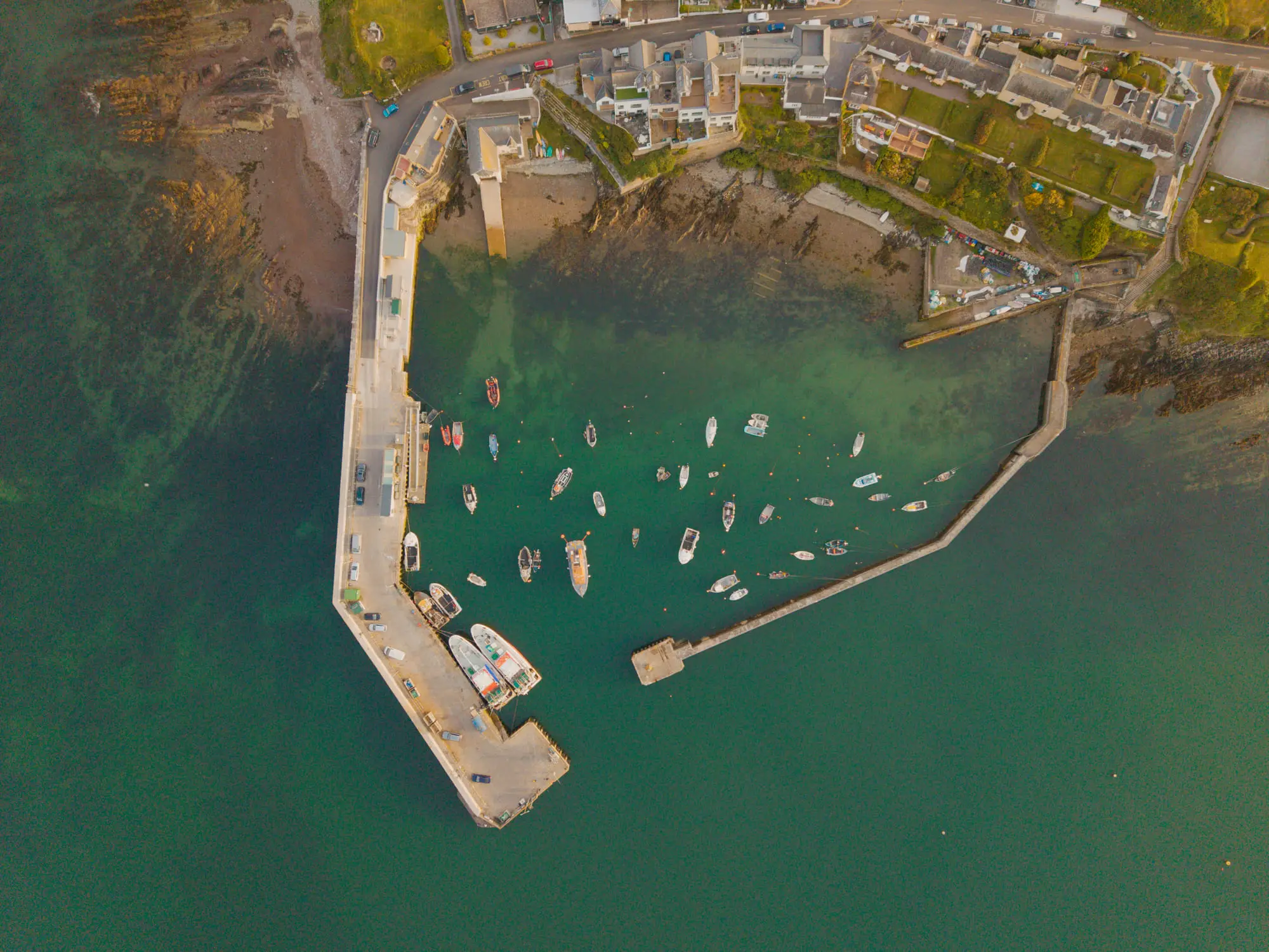 A stone pier and moored boats over turquoise water, aerial