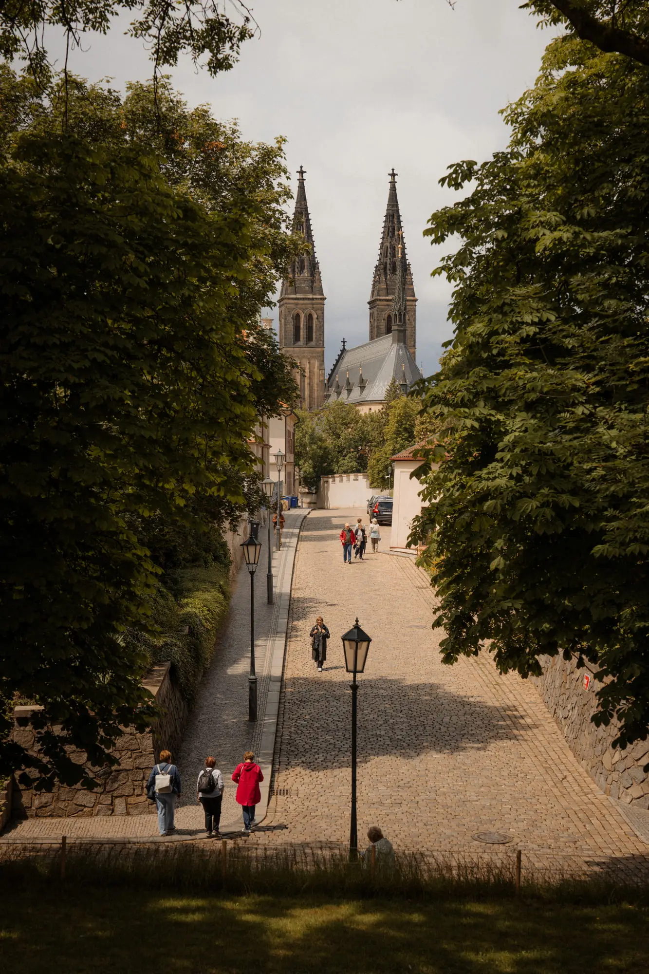 A lamplit cobbled avenue climbing toward the twin spires at Vysehrad