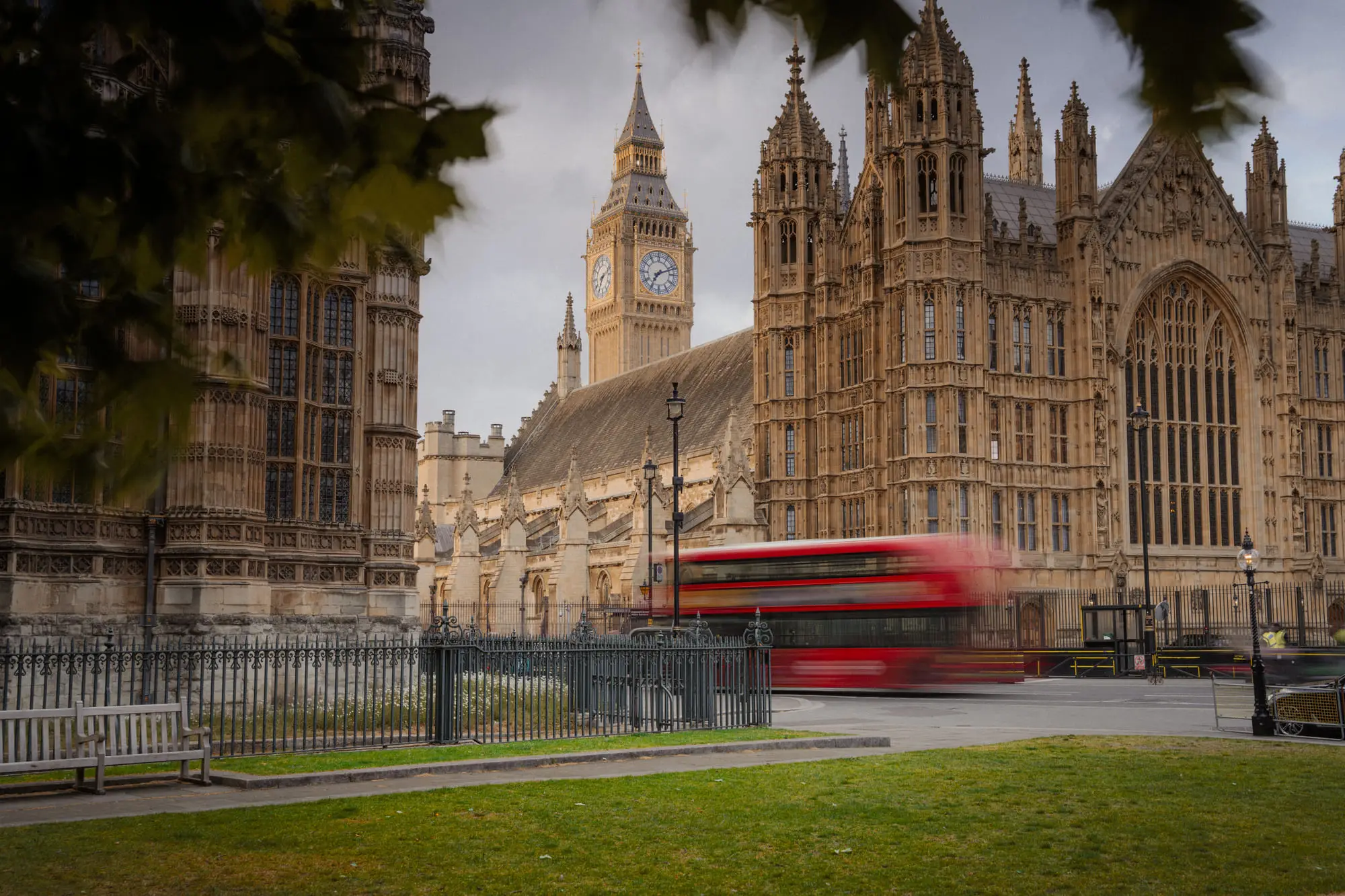 Westminster through autumn leaves, a red bus streaking past