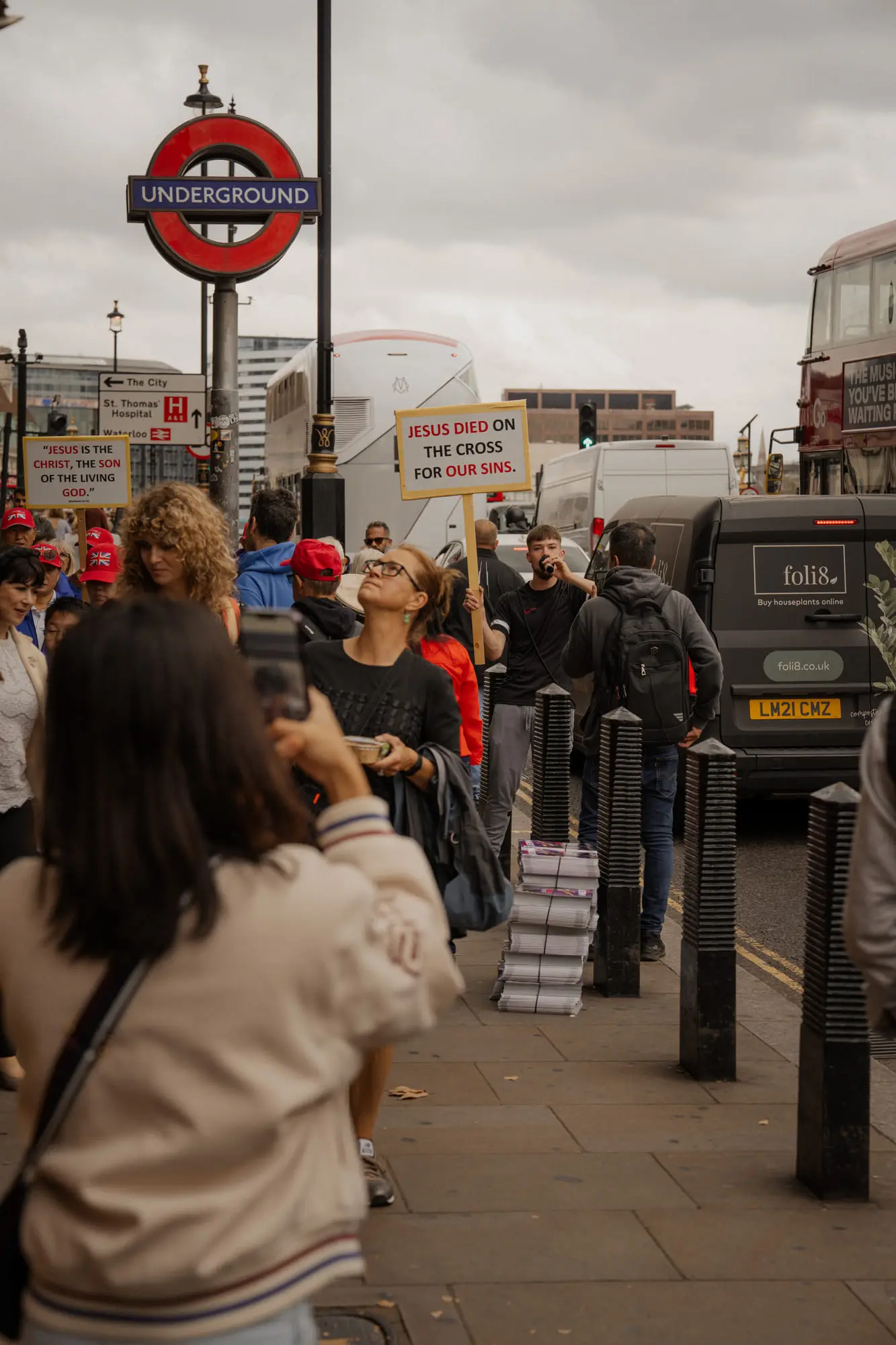 A placard under the Underground roundel, a passer-by taking a photo